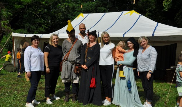 Wspólne zdjęcie grupowe kilku osób - pracowników Ośrodka Kultury i osób w średniowiecznych strojach, na tle białego namiotu.